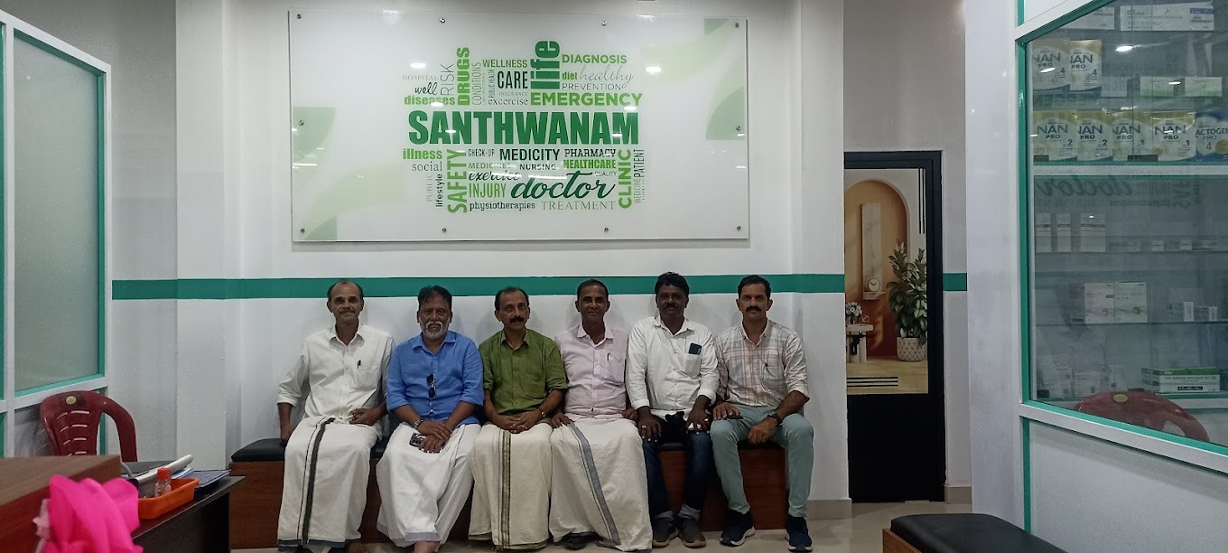 The Santhwanam Medicity team seated together beneath the green SANTHWANAM MEDICITY wall, with pharmacy shelves alongside.